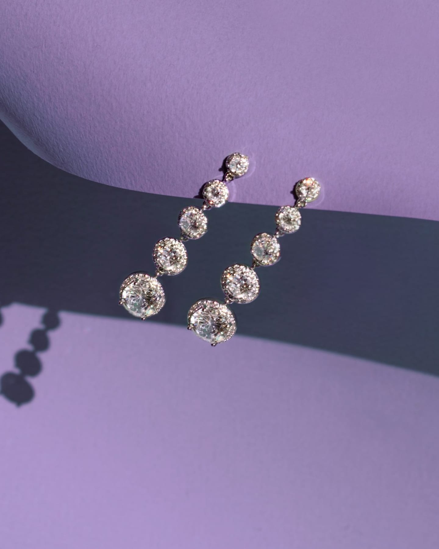 Graduated diamond drop earrings in white-metal settings on a purple background.