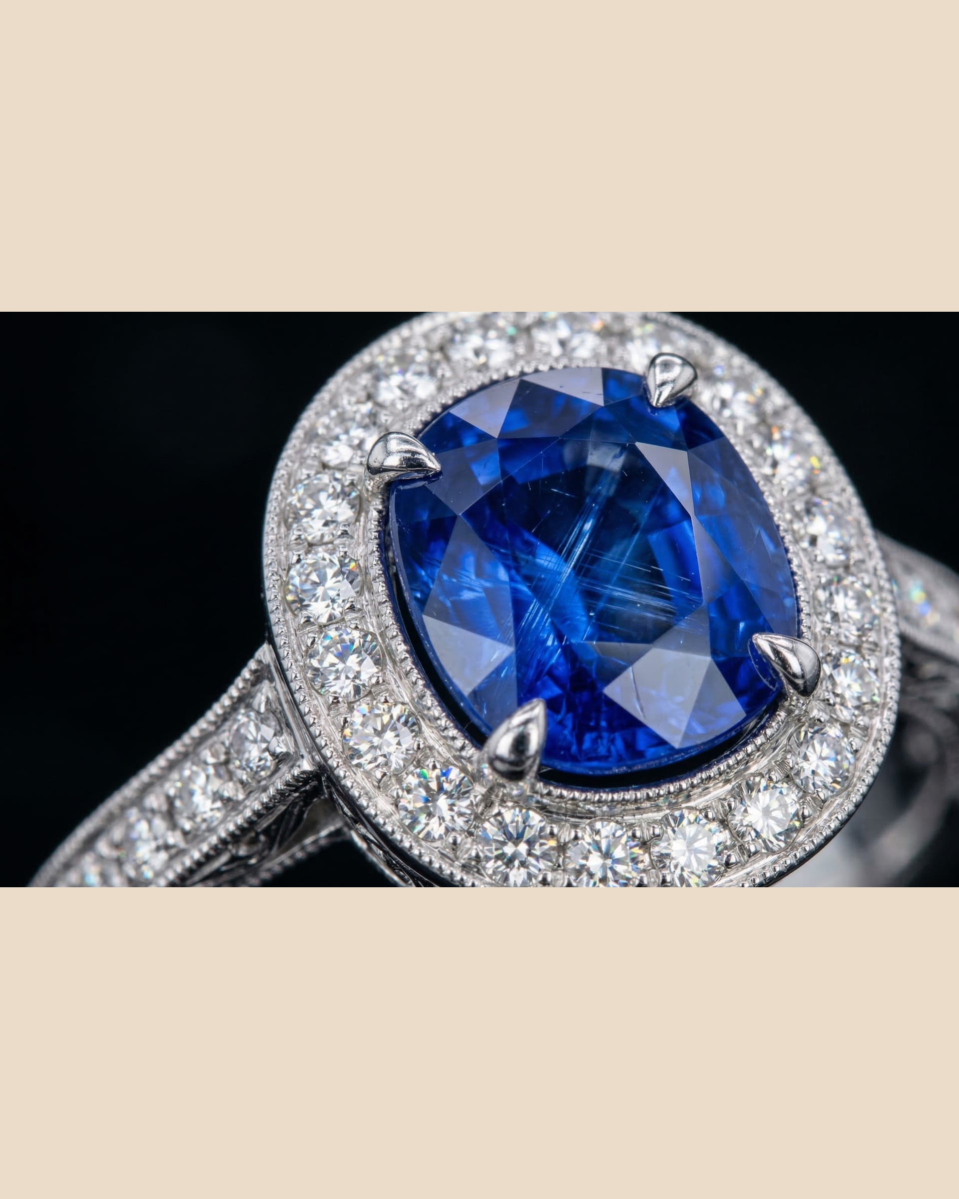 Oval blue sapphire ring with a close diamond halo and diamond-set shoulders.
